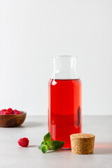 Raspberry drink in the glass bottle on the light background.