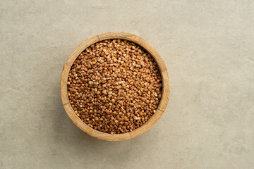 buckwheat in a wooden plate with a spoon on a gray stone background