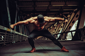 Young strong man bodybuilder posing on urban industrial background - obrazy, fototapety, plakaty