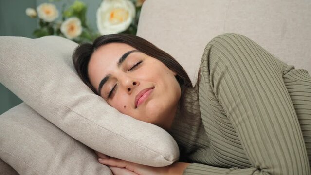 Sleeping caucasian young woman taking nap on the sofa during the day. Exhausted female napping at living room couch, having a good dream with positive expression. Paceful lady resting at home.