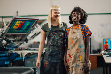Interracial female graphic industry workers at printing shop smiling.
