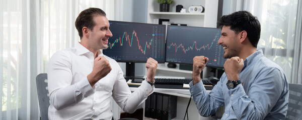 Cheerful two stock exchange traders raising fist up for digital achievement with panorama view on...