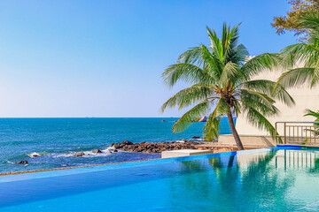 View of the outdoor pool by the sea. There is a lush palm tree next to the pool. Sanya, China.