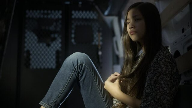 Scared girl looks around while sitting in a dark vehicle