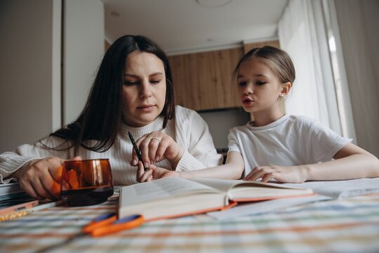 daughter doing homework together with young mother at home at kitchen table