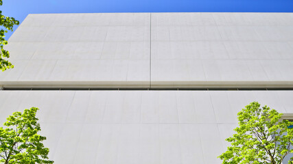 Modern white concrete building walls against blue sky. Eco architecture. Green trees and concrete office building. The harmony of nature and modernity.
