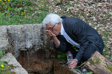 Man filling water by hand from a fountain in nature.