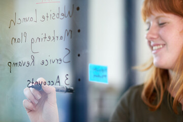 Happy woman, brainstorming or writing ideas on glass board or sticky note, planning in office. Creative project, agenda or designer in startup for working, strategy and storyboard with goals or smile