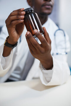Close-up shot shows a black man wearing a lab coat and clutching a prescription pill. Selective focus of an African American physician holding a bottle of medication for patient treatment.