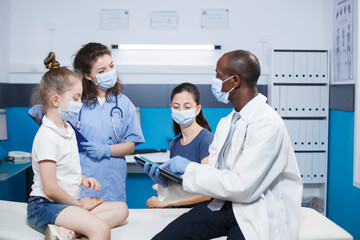 Obraz premium Doctor and nurse conducting a checkup, providing advice to a girl and her mother in a medical office. Healthcare professionals have a consultation with patients. Face masks worn for protection.