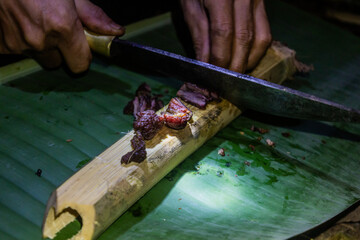 Local guide utting smoked meat on a bamboo in the forest near Luang Namtha, Laos