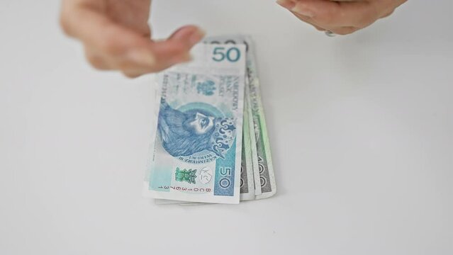 A person counting polish currency in an office setting, focus on hands and zloty bills