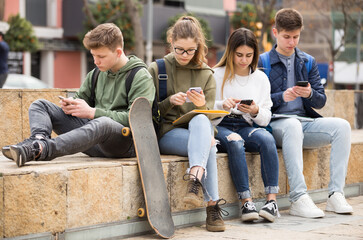 Teenage friends spending time together using smartphones outdoors