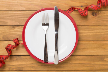 Measuring tape with empty plate on wooden background, top, view. Weight loss concept