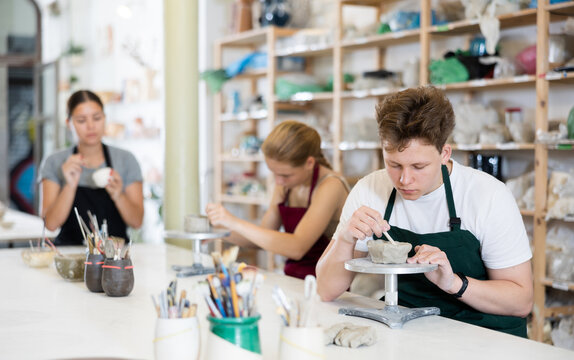 Young man in apron modeling clay pottery in workshop