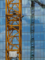 The shaft of a construction crane against the background of the modern glass facade of the building.