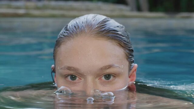 Woman looks at the camera while submerging her face underwater in a pool