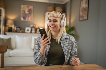 Young woman with headphones listen music and watch mobile phone happy - obrazy, fototapety, plakaty