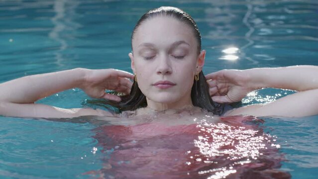 Woman in a pink silk gown emerges from the water in a swimming pool
