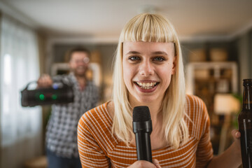 Adult woman sing karaoke on microphone with man in the background