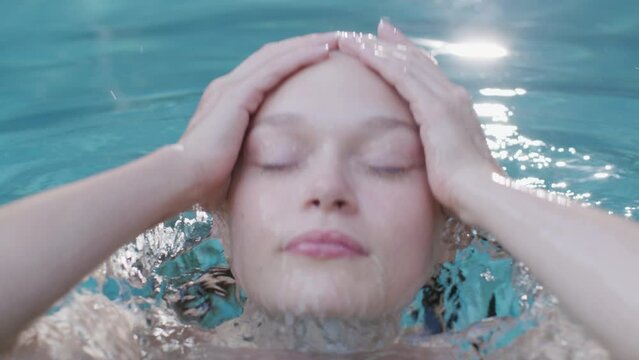 Woman wearing a pink gown looks at the camera while submerging her face 