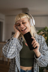 Young woman with headphones listen music and sign on mobile phone happy - obrazy, fototapety, plakaty