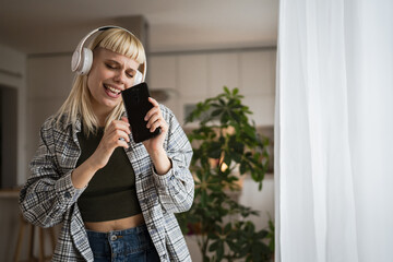 Young woman with headphones listen music and sign on mobile phone happy
