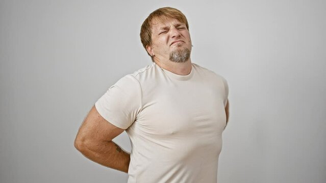 A young bearded blond man winces in pain against a white background, suggesting discomfort.