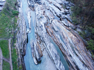 An aerial photo of a dry riverbed with boulders, trees, and a stream.