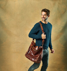 Fashion, thinking and smile of man in studio with leather bag isolated on a brown background mockup...