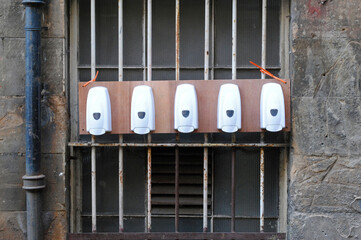 Row of Hand Sanitizer Dispensers on  Steel Bars of Old Window in Close Up