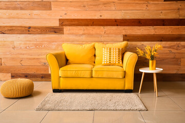 Modern yellow sofa with pillow, ottoman and coffee table near wooden wall