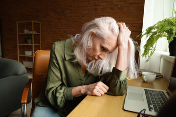 Depressed mature woman sitting near table at home