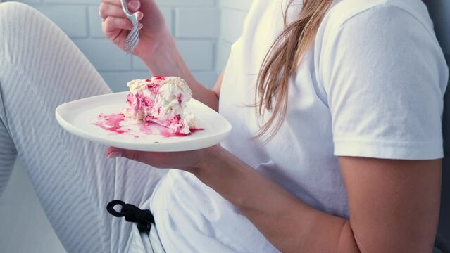 woman eating Meringue roll cake with cream and raspberries sitting in small balcony in the apartment
