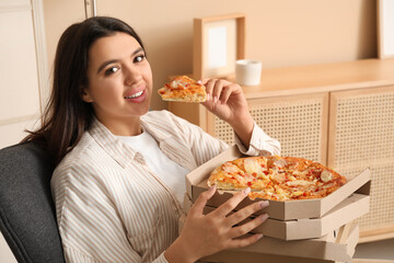 Young woman eating piece of tasty pizza and holding cardboard boxes at home