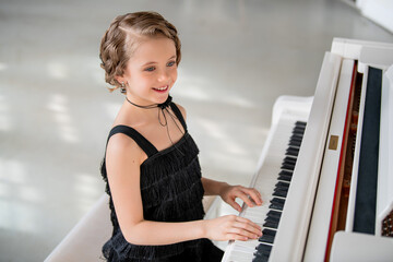 A young girl is playing the piano in a black dress.