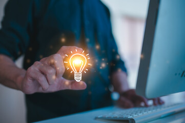 Creative businessman using computer and holding a virtual light bulb, representing a bright idea innovation and successful profit in global business