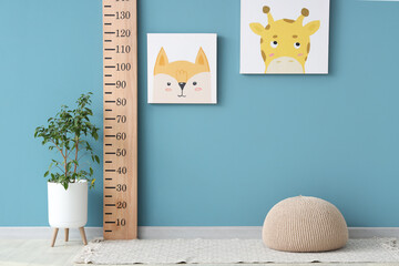 Wooden stadiometer with cute animal paintings and houseplant near blue wall