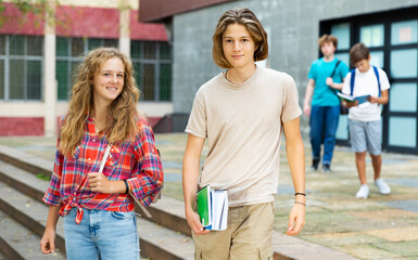 Two positive teens walk along summer street after finishing college lessons