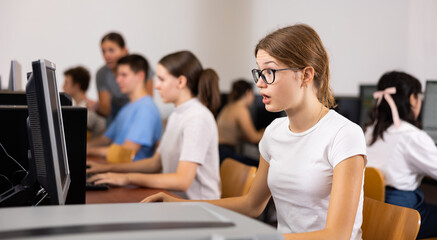 Focused female student in glasses using PC and studying computer science in the classroom