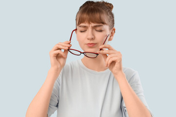 Tired young woman in eyeglasses on light background. Glaucoma awareness month