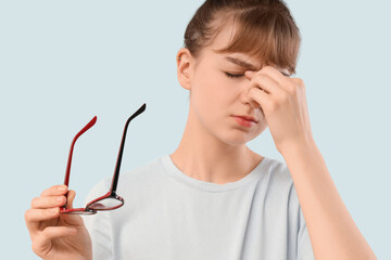 Tired young woman in eyeglasses on light background, closeup. Glaucoma awareness month