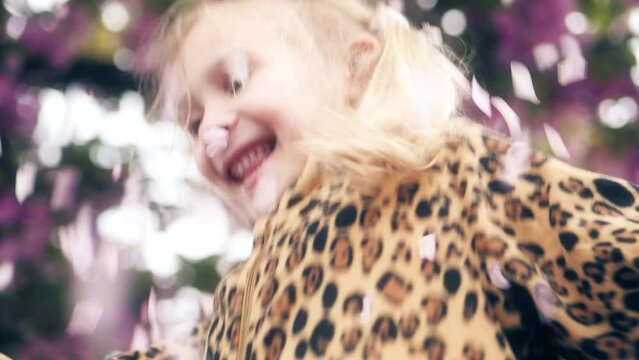 Happy little blonde girl jumps on pink tree flowers background