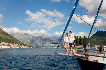 Traveling on yacht at sea. Happy couple having adventures. Travelers sailing, enjoying summer vacation. Tourists sightseeing on sailboat. Gorgeous landscape with beautiful mountains, Perast Montenegro