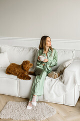 A Beautiful young woman with a golden brown labradoodle dog in living room at home , morning coffee. Cute Family puppy and girl play at home, decorated interior on holidays..