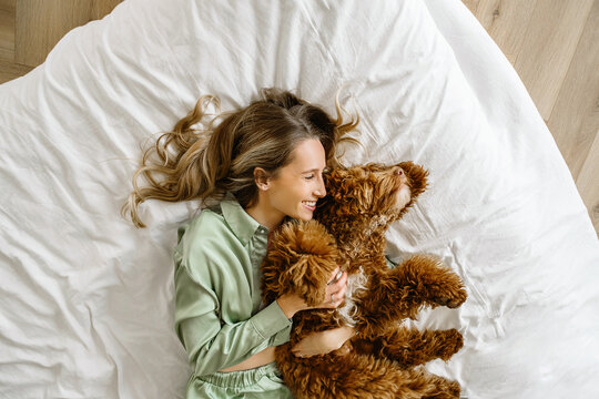 A Beautiful young woman with a golden brown labradoodle doglying in bed in bedroom at home , morning coffee. Cute Family puppy and girl play at home, decorated interior on holidays..