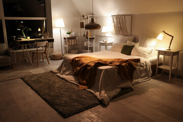 Interior of bedroom with workplace and glowing lamps at night - obrazy, fototapety, plakaty