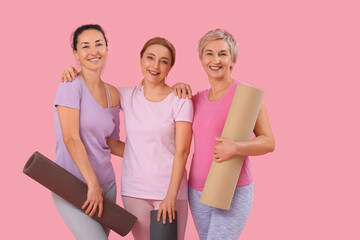 Mature women with yoga mats on pink background