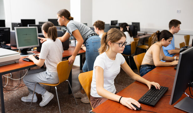 Clever teenage caucasian girl learning to use personal computer during lesson in school.