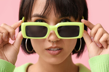 Stylish young woman in sunglasses with nose piercing on pink background, closeup